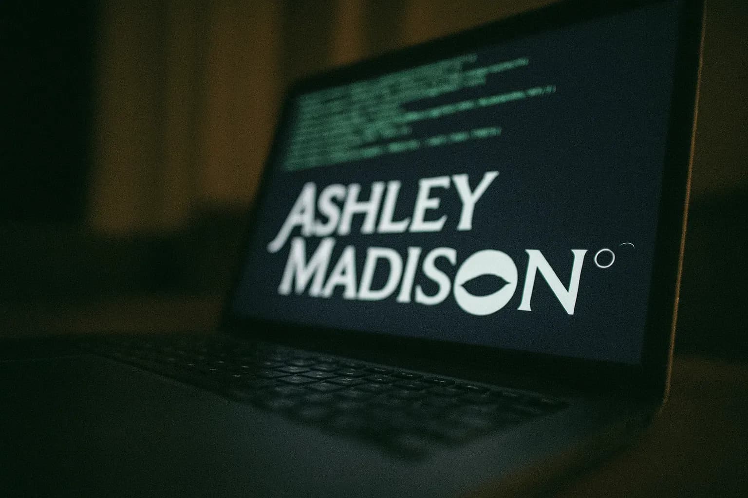 En laptopskærm viser Ashley Madison-logoen blandt kodelinjer, hvilket symboliserer databruddet i 2015, der afslørede millioner af brugere og førte til global afpresning og personlige tragedier.
